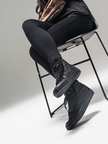 Model seated in a chair wearing black and camouflage DEFCON Syndicate SK8-Lo shoes, with the outsole visible.