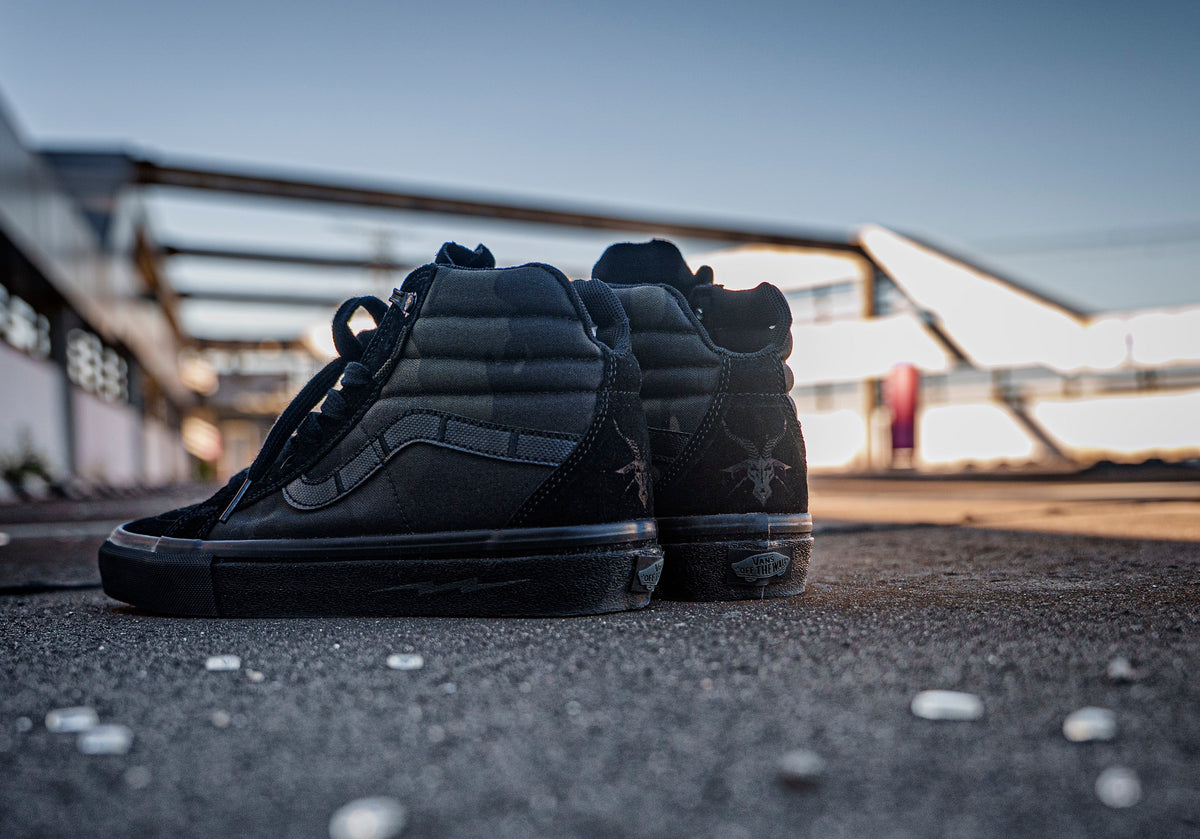 Pair of black DEFCON Syndicate SK8-Lo Notchback shoes placed on rooftop pavement in warm evening light.