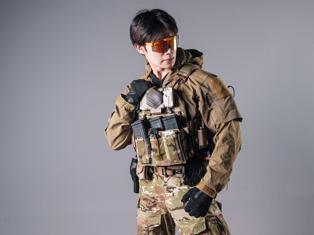 Model wearing the tan Gryphon Crocodile Halfshell Jacket with a camouflage chest rig and magazine pouches.