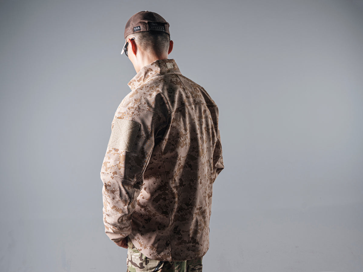 Front view of a model wearing the tan AOR1 digital camouflage Minotaur softshell jacket open over a black shirt.
