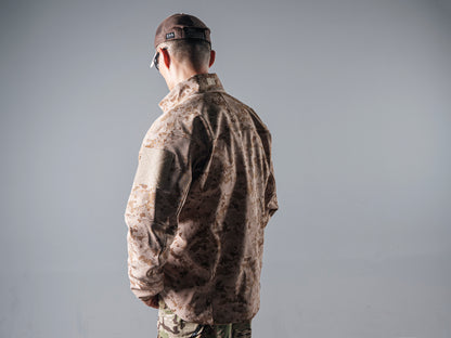 Front view of a model wearing the tan AOR1 digital camouflage Minotaur softshell jacket open over a black shirt.