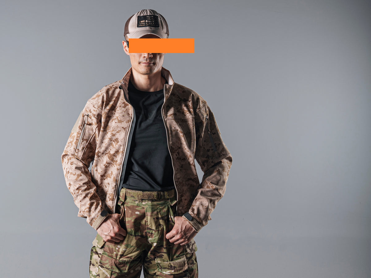 Front view of a model wearing the tan AOR1 digital camouflage Minotaur softshell jacket partly unzipped over a black shirt.