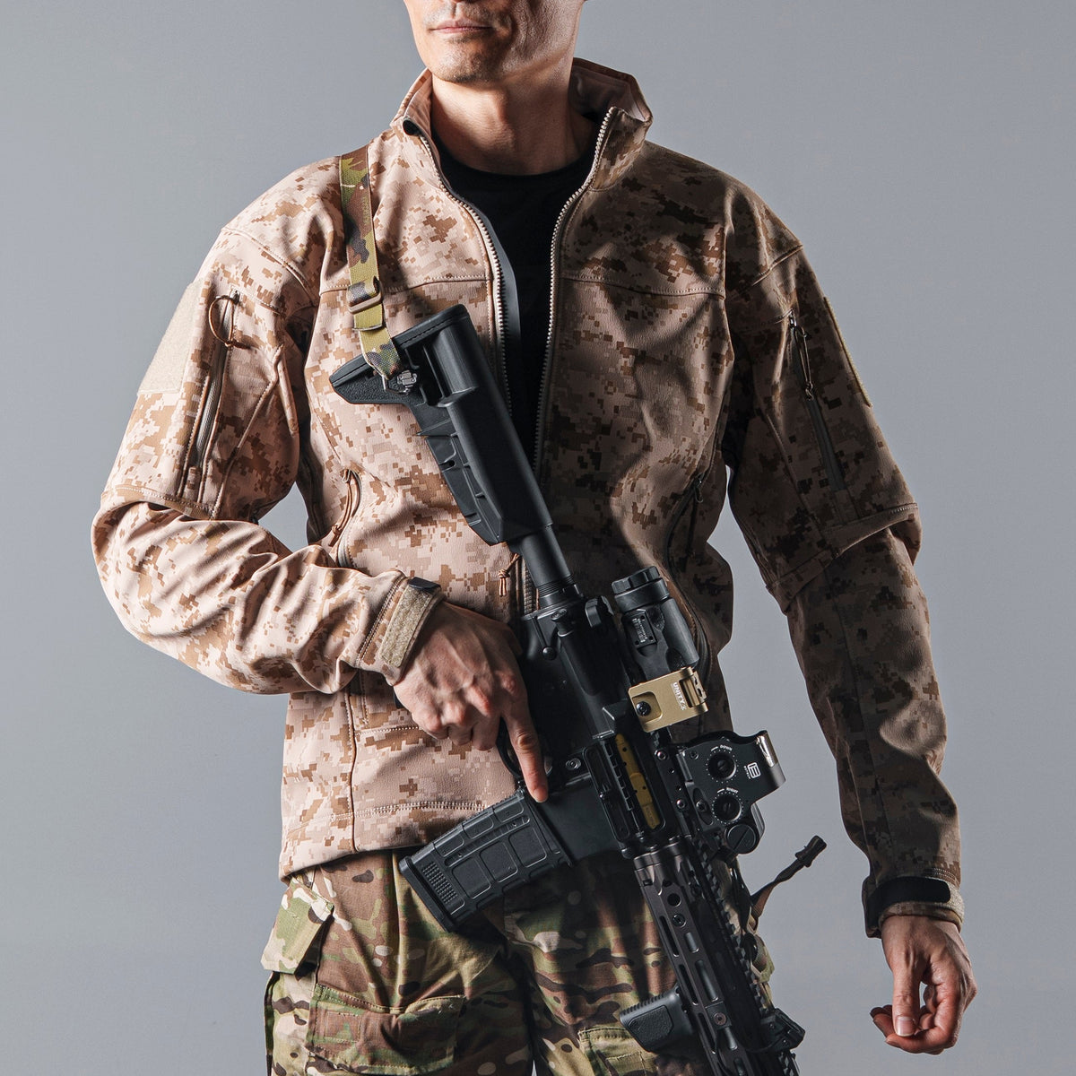 Model wearing the BKG ARC-Style LEAF Minotaur AOR1 softshell jacket with a front zip while holding a rifle.