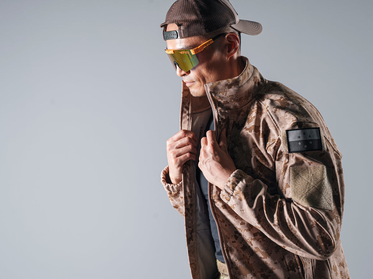 Close side view of the tan AOR1 Cold Fusion jacket as a model adjusts its raised collar.