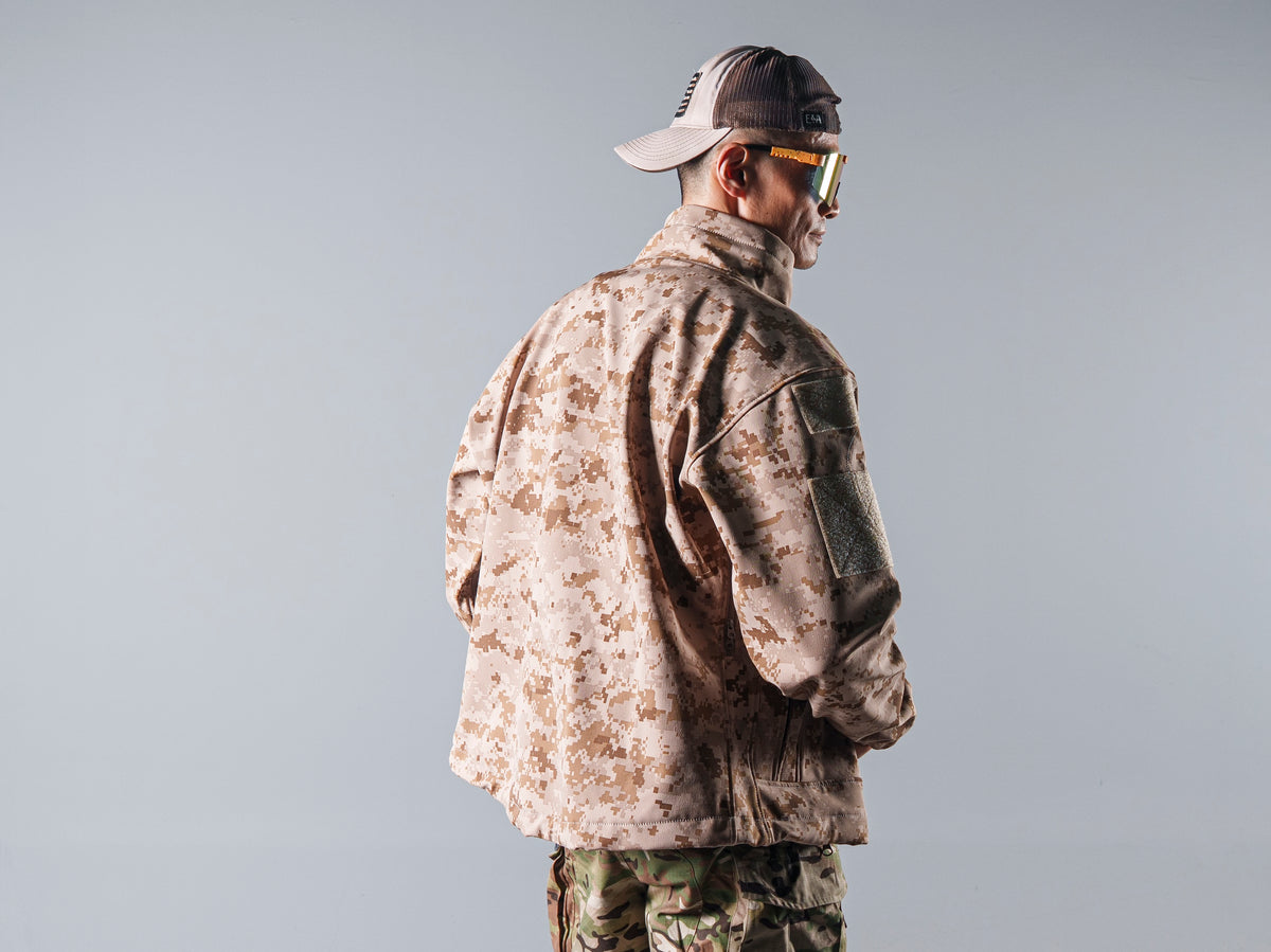 Rear view of a model wearing the tan AOR1 Cold Fusion softshell jacket with its raised collar.
