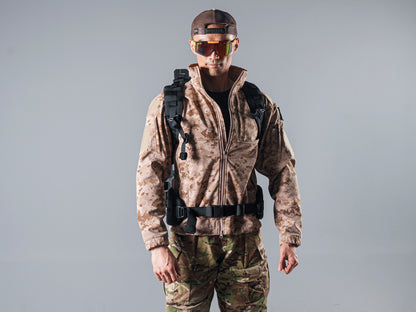 Front view of a model wearing the tan AOR1 Cold Fusion softshell jacket with black backpack straps and a waist belt.