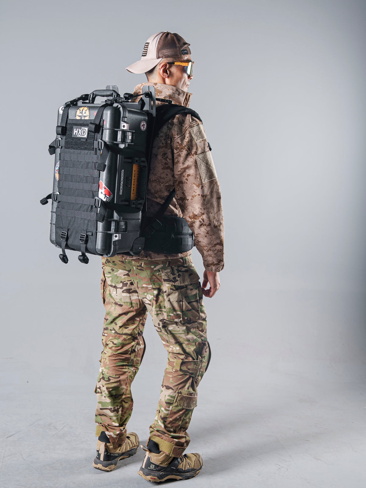 Rear view of a model wearing the tan AOR1 digital camouflage BKG BE-Style Cold Fusion jacket with a black hard-shell pack.