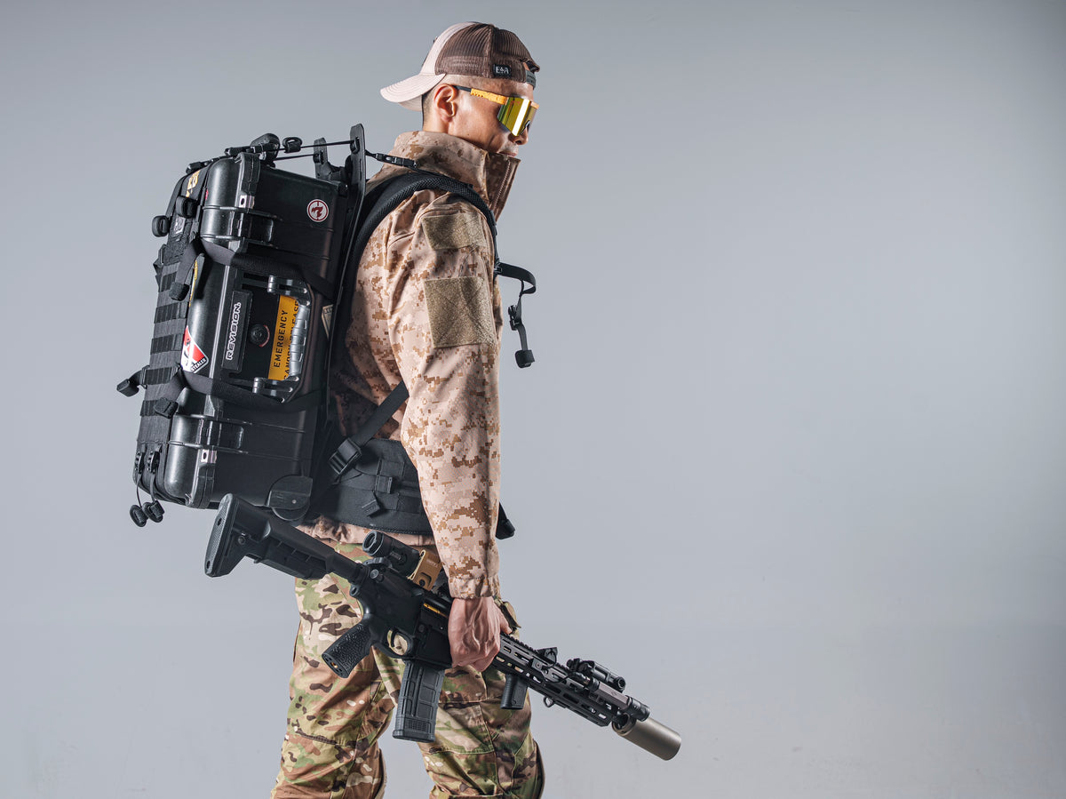 Side profile of a model wearing the tan AOR1 Cold Fusion softshell jacket with a large black pack and rifle.
