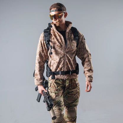Model wearing the tan AOR1 digital camouflage BKG BE-Style Cold Fusion softshell jacket with a black tactical backpack and waist belt.