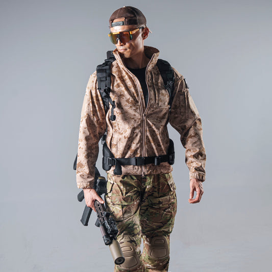 Model wearing the tan AOR1 digital camouflage BKG BE-Style Cold Fusion softshell jacket with a black tactical backpack and waist belt.